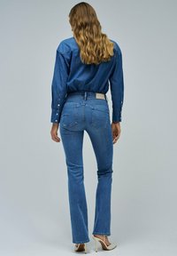 Modre flare kavbojke s srednje visokim pasom, ki imajo zadnje žepke in oznako na pasu. Oblečene so z dolgim denim srajcami.