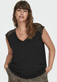 Top nero senza maniche con scollatura a V, con dettagli in pizzo sulle spalle. Indossato con pantaloni a stampa leopardata, che mostrano una vestibilità comoda.