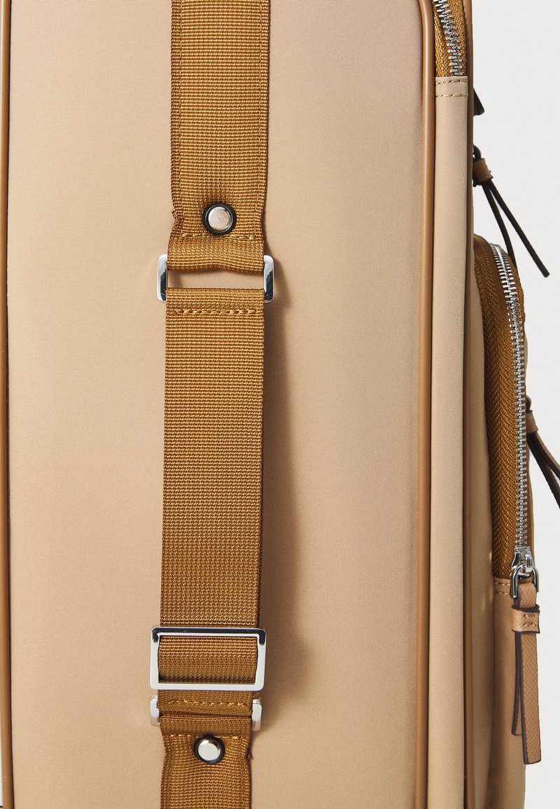 Beige travel bag featuring a textured exterior, a brown nylon strap with a silver buckle, and a side zip pocket.