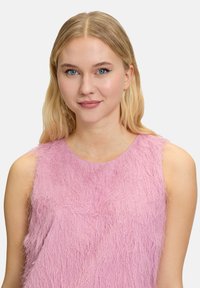 Top sans manches en rose doux avec une texture duveteuse. Présente un encolure ronde et une coupe ample, mettant en valeur un design vibrant et superposé.