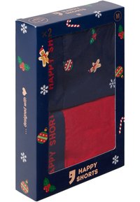 Två par shorts i en låda. Ett i rött och ett i marinblått med festliga mönster, inklusive pepparkaksgubbar och dekorationer, med en glansig yta.