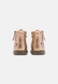 Brązowe syntetyczne botki o gładkiej fakturze, z zamkami błyskawicznymi z tyłu, perforowanymi detalami i grafiką postaci z boku.