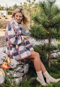 Fleece jacket in cream, blue, and pink check pattern; relaxed fit with buttons. Model holding gray wallet, wearing beige ankle boots.