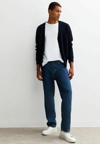Marinblått ribbat cardigan över en vit t-shirt, med blå raka jeans och vita sneakers. Enkel design med en avslappnad passform.