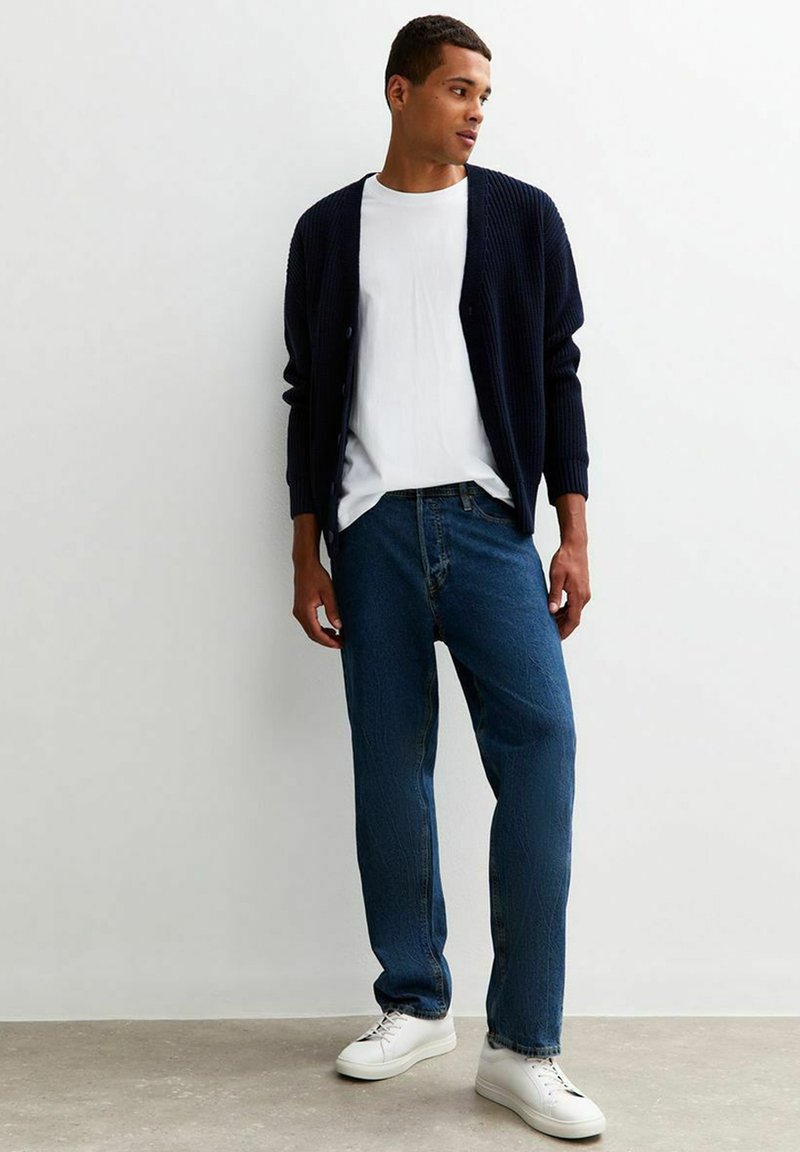 Marinblått ribbat cardigan över en vit t-shirt, med blå raka jeans och vita sneakers. Enkel design med en avslappnad passform.