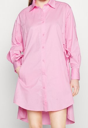 Lyserød skjortekjole med lange ærmer, brystlomme og bindedetaljer på ærmerne. Fremstillet af glat stof med en løs pasform.