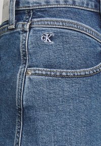 Džínové kalhoty Calvin Klein ve středně modré s texturovaným povrchem. Obsahují malé bílé logo na zadní kapse a stříbrné kovové doplňky.