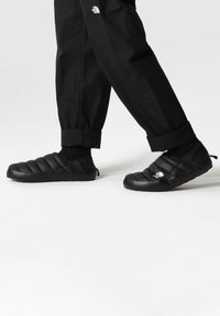 Black slip-on shoes with quilted design and rubber sole. Features logo on side, textured accents, and a lightweight construction.