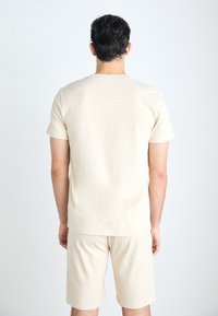 Camiseta de manga corta beige y pantalones cortos hechos de tela suave, con un ajuste relajado. La prenda presenta un diseño simple sin patrones visibles.