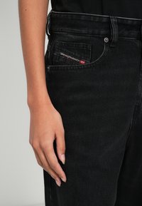 Μαύρα τζιν από τζιν ύφασμα με ίσια γραμμή στο παντελόνι, που διαθέτουν μια μικρή κόκκινη και λευκή ετικέτα με το λογότυπο στην εμπρόσθια τσέπη και μι�α υφή με ανάγλυφη επιφάνεια.