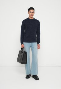 Navy textured long-sleeve sweater, light blue wide-leg jeans, black leather tote bag, and black shoes. Minimalist, modern design.