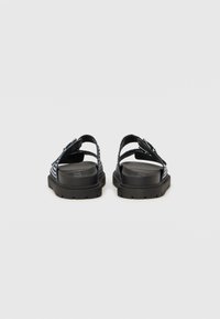 Sandali neri con apertura sul retro, dotati di cinturini in tessuto con un motivo intrecciato, suole in gomma e fibbie regolabili per una vestibilità sicura.