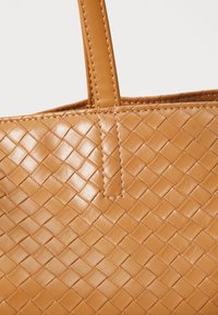 Geweven tan leren tote bag met een gladde textuur, met een naadloos ontwerp en bijpassende tan stiksels op de handgrepen en het lichaam.