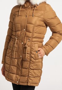 Brown puffer coat with a fur-lined hood, featuring a zip closure, drawstring waist, and angled pockets with decorative buttons.