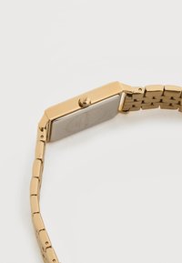 Ορθογώνιο ρολόι χειρός σε χρυσό χρώμα με συνδεδεμένο βραχιόλι, κορώνα στο πλάι και πίσω πλακέτα από ανοξείδωτο ατσάλι πάνω σε λευκή επιφάνεια.