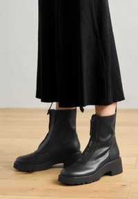 Black leather ankle boots with a chunky platform sole and a front zipper. Smooth texture with a minimalistic design.