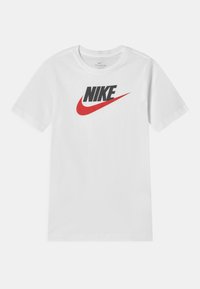 Camiseta blanca de manga corta hecha de algodón con cuello redondo. Presenta un logotipo negro de "NIKE" y un gráfico de swoosh rojo en la parte frontal.