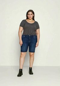 Szürke, testhez simuló póló, sötétkék farmer rövidnadrág és fekete bokacsizma. A rövidnadrág közepes magasságú derékkal és elülső zsebekkel rendelkezik.