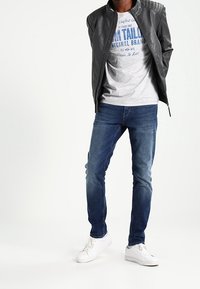 Herroutfit som består av en svart läderbomberjacka, grå grafisk t-shirt, blå denimjeans och vita sneakers.