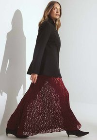Blazer negro ajustado combinado con una falda maxi de encaje burdeos, que presenta un diseño en capas, un ajuste de cintura alta y una silueta fluida.