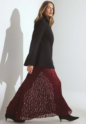Blazer nero aderente abbinato a una gonna lunga in pizzo borgogna, con un design a strati, vita alta e silhouette fluida.