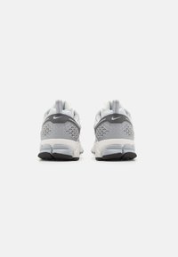 Chaussures de sport grises et blanches avec une tige en maille, une semelle intermédiaire texturée et une semelle extérieure noire contrastante ; présente un motif circulaire à l'arrière.