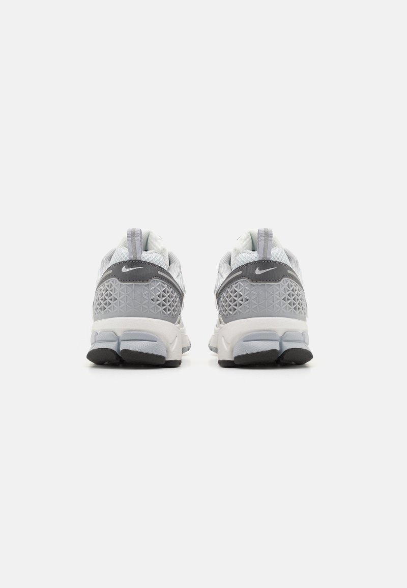 Grijze en witte sportschoenen met een bovenwerk van mesh, een getextureerde tussenzool en een contrasterende zwarte buitenzool; heeft een cirkelpatroon aan de achterkant.