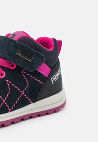 Chaussure en suède et en tissu bleu foncé avec des accents roses, présentant un motif de couture diagonale texturé et une semelle en caoutchouc moulé. Étiquette Gore-Tex incluse.