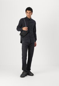 Čierna kockovaná košeľa na button-up, tmavé džínsy, šedé tenisky a malá čierna crossbody taška. Hladká tkanina a voľný strih.