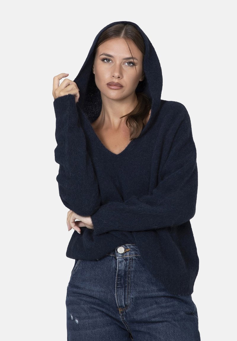 Maglione con cappuccio blu navy a V, realizzato in morbido tessuto testurizzato, con maniche lunghe e un taglio casual. Abbinato a jeans strappati.