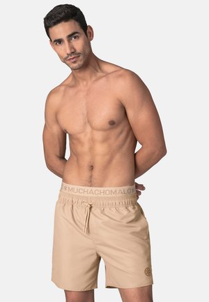 Beige színű úszónadrág húzózsinórral, márkás derékrésszel és kis logó részlettel. Simaság jellemzi, közép-thigh hosszúságú.
