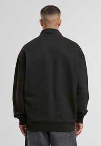 Black sweatshirt with a high collar, relaxed fit, ribbed cuffs and hem, made of textured cotton blend fabric, shown from the back.