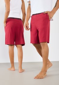 Røde bomullshorts med elastisk midje og svarte detaljer. Designet inkluderer lommer og en avslappet fasong, passende for fritidsbruk.