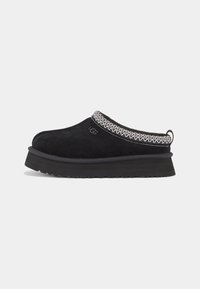 Black suede slip-on shoe with a thick sole, featuring an embroidered cuff and a discreet logo on the side. Minimalist design, soft texture.