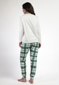 Top bianco a maniche lunghe con colletto rotondo abbinato a pantaloni a quadri verdi e blu. I pantaloni presentano polsini elasticizzati e una vestibilità comoda.