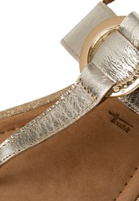 Remskandal med metallisk silverfärgad konstläder, en stor guldfärgad ringdetalj och en mjuk tanfärgad mockainläggssula med sömnadsdetaljer.