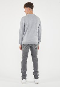 Maglietta grigia a maniche lunghe con scollatura a girocollo, abbinata a jeans grigi con cuciture decorative sulle tasche posteriori e sneaker bianche.