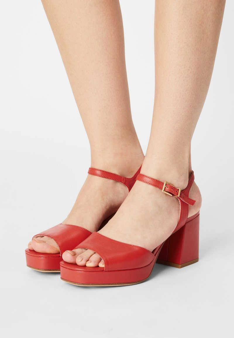 Sandales en cuir rouge à plateforme avec orteils ouverts, bride de cheville avec boucle en or et talon carré épais. Texture lisse et couleur unie.