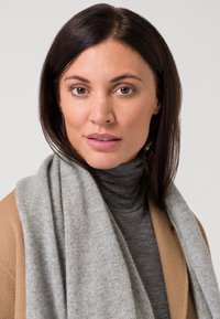 Gray knitted scarf draped over a gray turtleneck, paired with a tan coat. Smooth texture, warm materials, and neutral color palette.