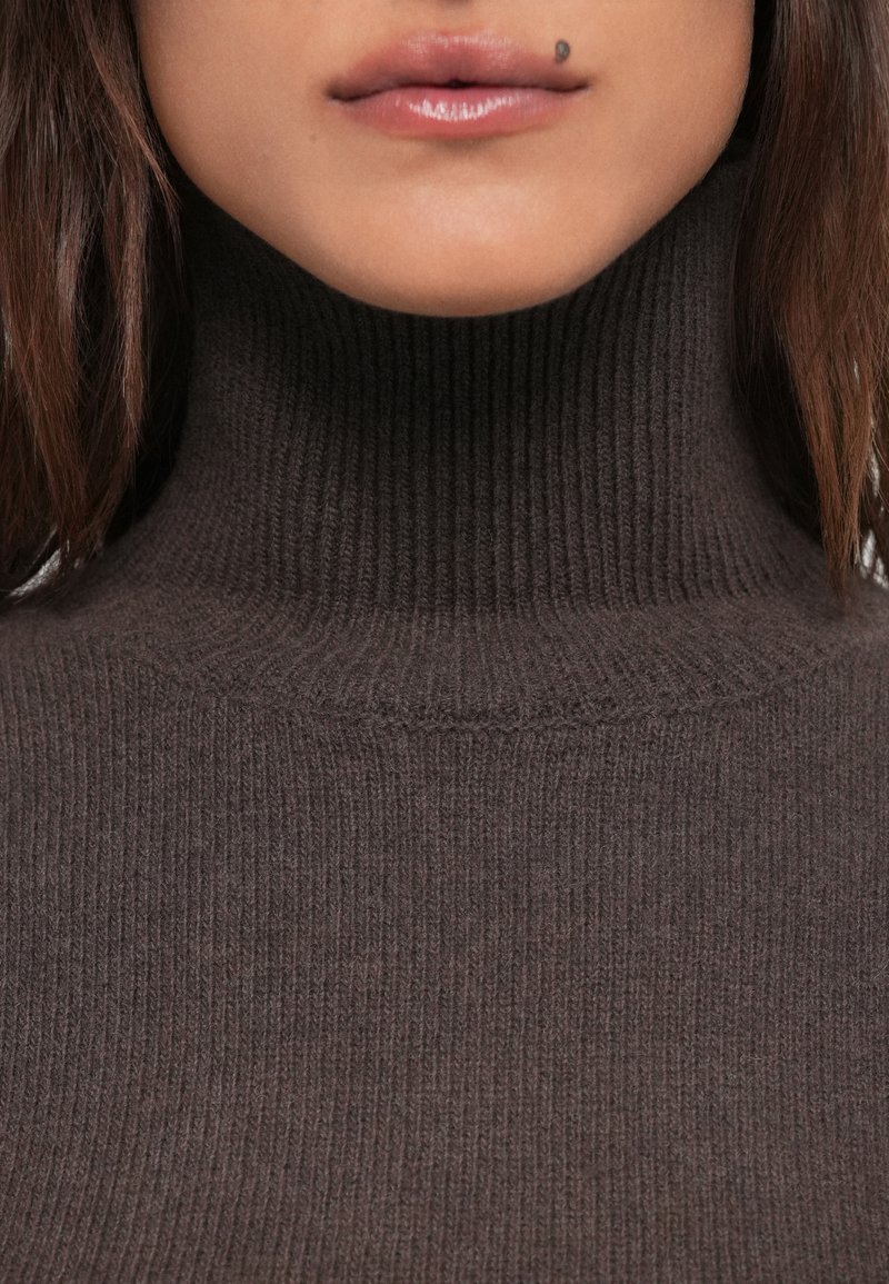 Brown ribbed turtleneck sweater with a fitted design and soft texture, featuring a high collar and subtle horizontal ridges.