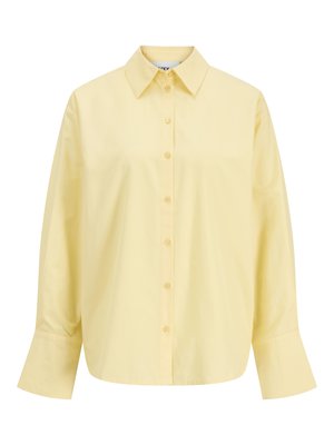 Hele kollane pikkade varrukatega nööpidega pluus, millel on laiad mansetid ja terav krae, esitatud valgel taustal.