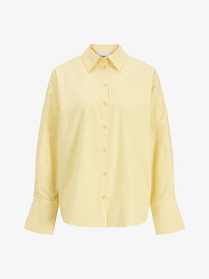 Hele kollane pikkade varrukatega nööpidega pluus, millel on laiad mansetid ja terav krae, esitatud valgel taustal.