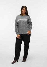 Suéter gris de punto con el texto "MON AMOUR" en blanco, combinado con pantalones negros y botines de tacón marrón, sobre un fondo blanco.