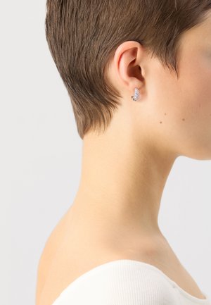 Orecchini in argento sterling con superficie testurizzata, con design a farfalla. Indossati con capelli castani corti su uno sfondo neutro.