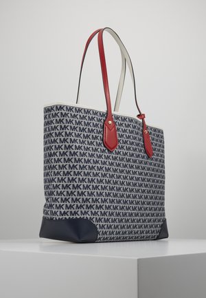 Borsa tote con motivo logo blu navy, angoli inferiori neri e doppi manici in pelle rossa su una superficie bianca espositiva.