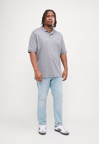 Polo grigio con colletto e maniche corte, abbinato a jeans azzurri chiari e sneakers bianche con dettagli neri. Design semplice.
