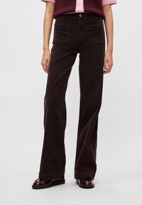 Καφέ παντελόνι καμπάνα από κορδούρα με ψηλή μέση, διαθέτοντας μπροστινές τσέπες και υφή στην επιφάνεια, σε συνδυασμό με αμυγδαλωτό πλεκτό τοπ σε αντίθετο χρώμα.