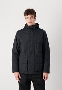 Veste noire imperméable avec une capuche, dotée de fermetures à bouton-pression, d'une poche poitrine et de deux poches inférieures, fabriquée à partir d'un matériau lisse et durable.