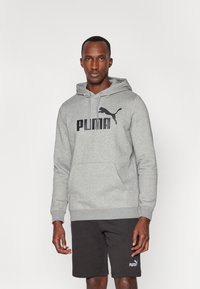Felpa grigia con un grande logo Puma nero, con cordini e una tasca frontale; abbinata a pantaloni corti neri con un piccolo logo.