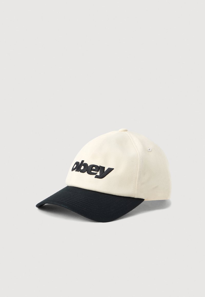 Béžová bavlnená čiapka s čiernym okrajom. Obsahuje logo "obey" v tučnom čiernom písmene. Zahrňuje odvetrávacie dierky a zaoblený dizajn koruny.